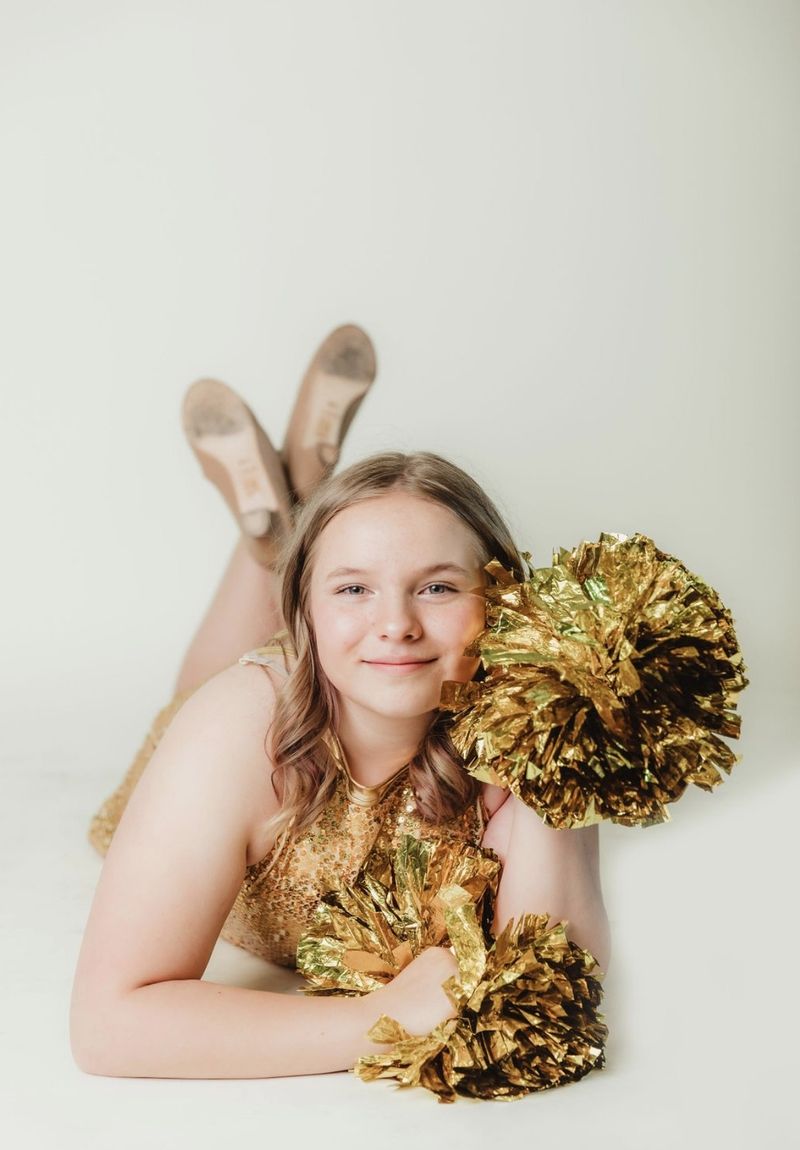 A DanceXplosion dancer in a gold sequin costume, smiling with gold pom-poms