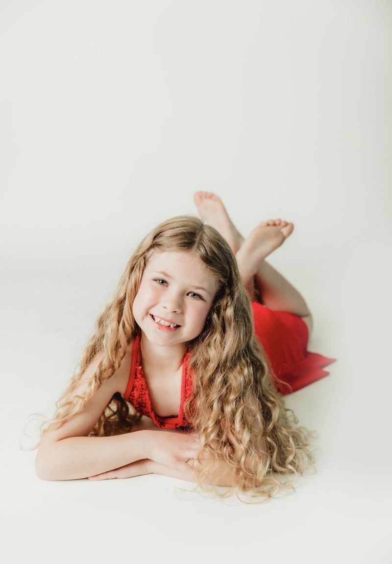A young DanceXplosion dancer in a red costume, grinning on the studio floor